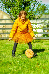 Young Girl in Yellow Puffer Jacket Raising Pumpkin in Lush Garden During Autumn