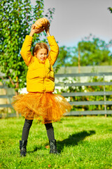 Young Girl in Yellow Puffer Jacket Raising Pumpkin in Lush Garden During Autumn
