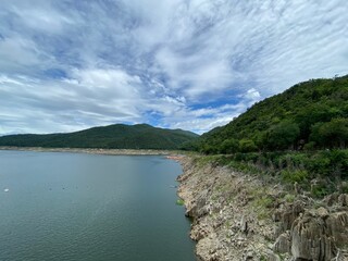 Scenic view of a dam in the mountains with a river, lush green trees, and a clear blue sky at Bhumiphol Dam, Tak, Thailand.
