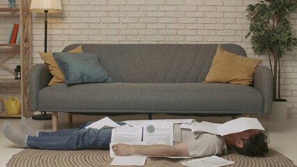 A young male college student lying on the floor of a room, doing homework or studying for exams....