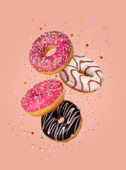 Donuts with sprinkles, pink and chocolate glaze fly on colorful pink background