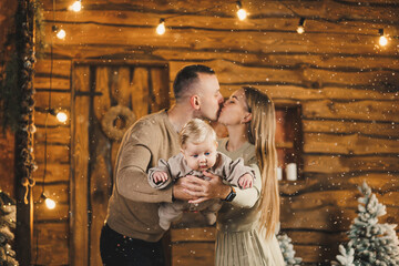 Young mother and father are playing with their child while sitting near the Christmas tree at home. Christmas family atmosphere