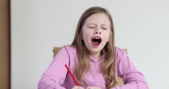 Junior schoolgirl performs homework yawning continuously sitting at desk slow motion. Sleepy girl with pencil in hand demonstrates fatigue