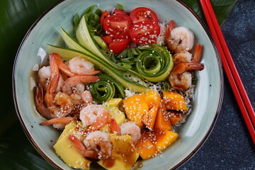 Fresh seafood recipe. Shrimps poke bowl with rice, green onions, tomatoes,avocado,mango. Food concept poke bowl on gray background
