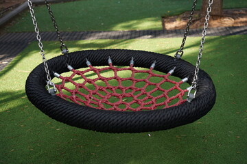 Round swing seat made of mesh in playground. Empty red rope web nest for swinging closeup. Wicker round swing in the park