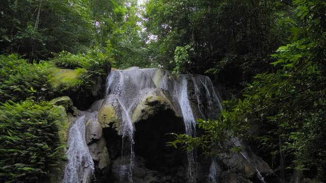 A breathtaking War Inkabom Waterfall on Batanta Island in Raja Ampat, Indonesia, cascades down a rocky cliff, surrounded by lush greenery. Tilt-down shot in slow-motion.