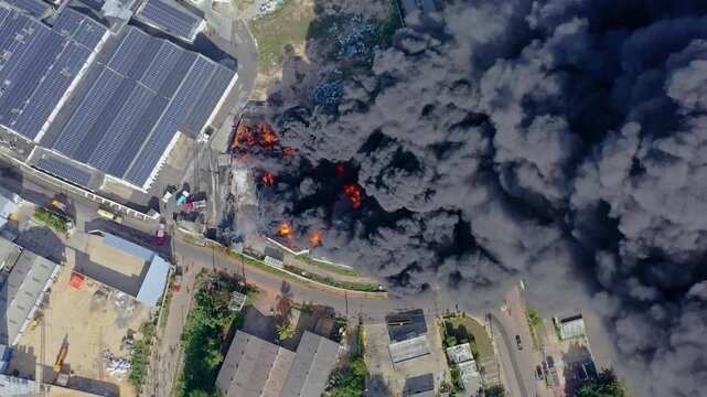 Thick black dangerous smoke fumes of burning factory, drone top down orbit