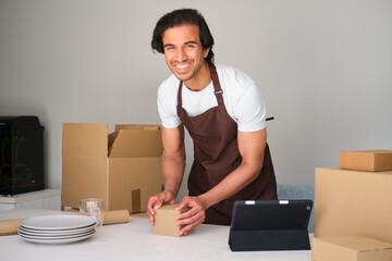 Happy small business owner packing a package while using a tablet