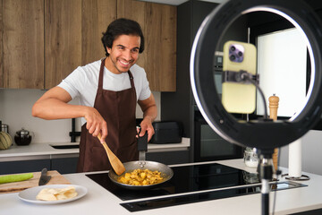 Man is preparing chicken curry in a modern kitchen and recording a video blog