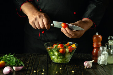 Preparing a salad with vegetables and cherry tomato. A chef cuts tomatoes for a vegetable menu on a pub kitchen table. Vegetable diet concept