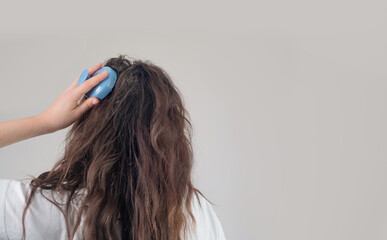 Naklejka premium Brunette with long, curly hair holds a head massager, performing a daily routine to boost hair growth.