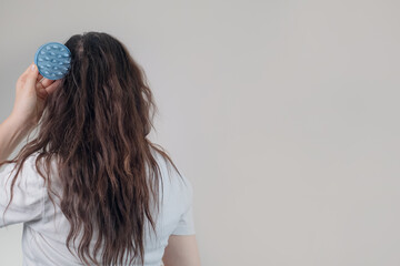 Caucasian woman holds a scalp massager, which may help reduce headaches and migraines by relaxing tense head and neck muscles.