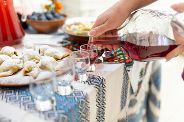 Tasting of sweet plum liqueur. A woman pours a drink from a carafe into liqueur glasses. Traditional treats in Ukrainian Pokut. Ivano-Frankivsk region, Ukraine.