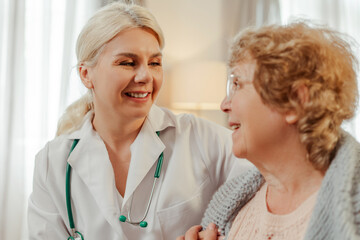 Fototapeta premium Female doctor smiling and comforting elderly female patient at home