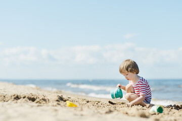 Cute little boy having fun on a sandy beach on warm and sunny summer day. Kid playing by the ocean. Summer activities for children