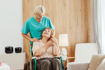 Nurse comforting smiling senior woman in wheelchair at home hugging, support