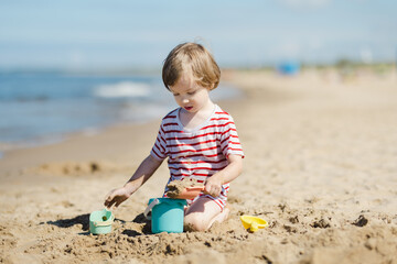 Cute little boy having fun on a sandy beach on warm and sunny summer day. Kid playing by the ocean. Summer activities for children