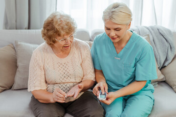 Nurse assisting senior woman using glucose meter at home