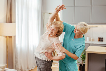 Physiotherapist assisting a senior woman stretching her back at home