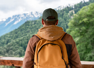 man with a yellow backpack in a cap enjoying a mountain view on a hike