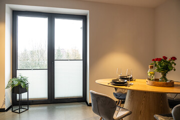 Interior of a Modern furnished Kitchen in a New House. Dining Table and Chairs in Stylish and Functional Space. Detailed kitchen Design. Dining table with plates, glasses and vase of red roses.