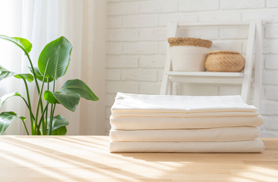 Pile of folded bed sheets on wooden table in bright house room