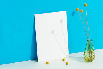 White blank paper mockup on blue background with billy buttons in a vase