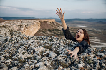 Empowered woman standing on mountain peak, shouting with arms raised in triumph