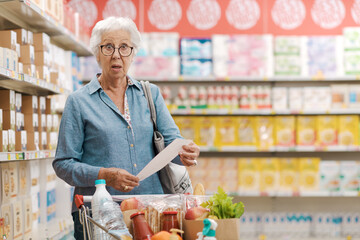 Shocked senior customer holding a long expensive grocery receipt
