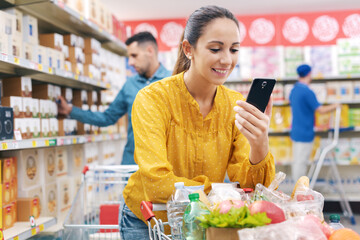 Woman buying groceries at the supermarket and connecting with her smartphone