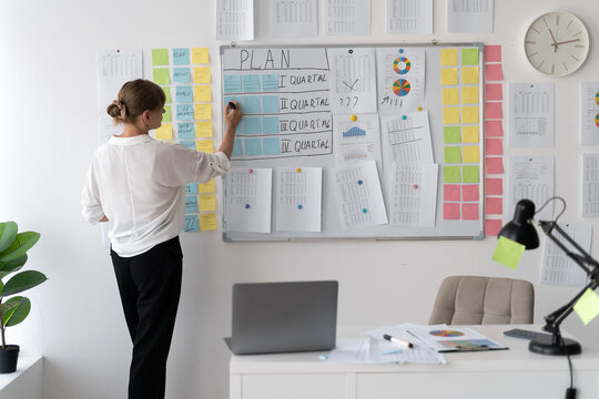 executive manager elderly businesswoman writing ideas on sticky notes on whiteboard doing business project presentation working in small office