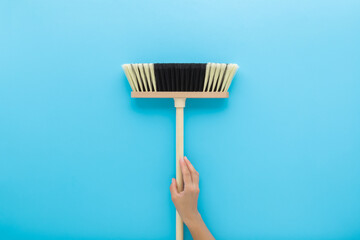 Young adult woman hand holding and showing new white black broom with wooden stick on light blue...