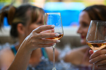 Two women are enjoying a relaxing soak in a hot tub, toasting with glasses of rose wine