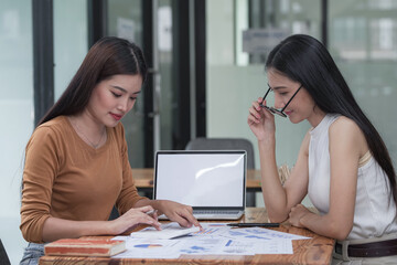 Two young Asian businesswomen discussed investment project work and planning strategy. Business people talk together on laptop computers at the office.