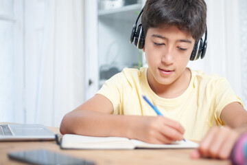 Naklejka premium Young student writing with a pen on a notepad on a desk. She is wearing a wireless headset.