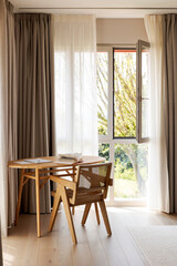 Wooden desk with an armchair in the bedroom. Windows covered by curtains. You can see the garden outside
