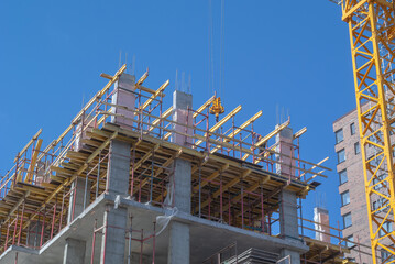 A tower construction crane lifts building materials to a height. The frame of a building under construction.  A construction load is attached to the crane hook.