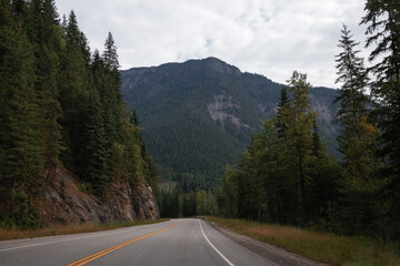 Canadian Rockies, summer vacation in British Columbia. Highway in the mountains with coniferous forest and cloudy sky. 