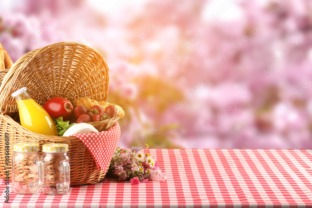 Poster Picnic basket with foods and juice on table in nature. Space for text