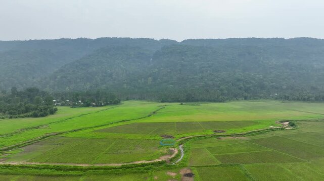 Aerial view of serene mountain valley with lush greenery, fields, and distant rolling hills enveloped in mist.