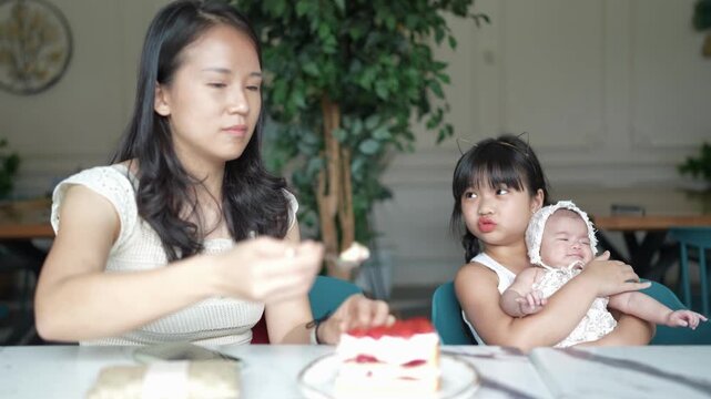 Slow-motion video of 20-something Chinese Malaysian woman in white clothes, 13-year-old girl in white dress, and newborn baby having conversation at table in stylish caf&eacute; in Selangor, Malaysia.