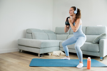 Young woman exercising at home with her pet. Listening to music with her headphones. Motivation to...
