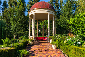 A large gazebo with columns in a picturesque park or city garden on a sunny summer day