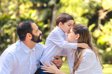 Brazilian family sharing a tender kiss outdoors. A young boy lovingly kisses his mother while the father looks on with pride and joy. Perfect for themes of love, family, and heartfelt moments