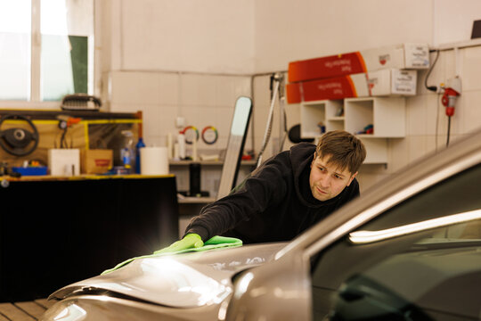 Man polishing car hood in garage, enhancing automotive exterior design