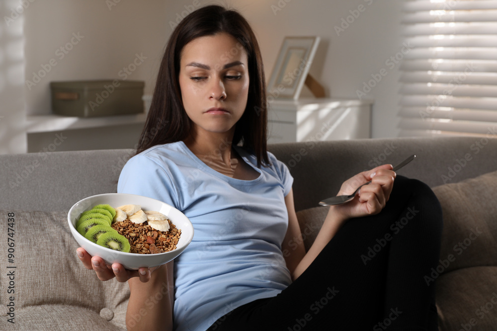 Poster Eating disorder. Sad woman with spoon and healthy meal on sofa indoors