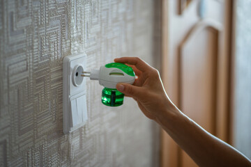 Person hand plugs mosquito repellent into the socket before going to bed. Domestic electric raptor...