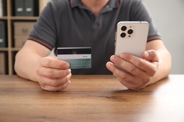 Man with credit card and smartphone at wooden table indoors, closeup