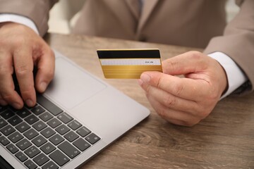 Man with credit card using laptop at wooden table, closeup