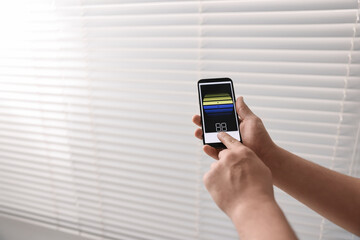 Man using phone to adjust window blinds indoors, closeup. Space for text